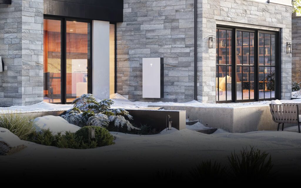 Modern stone clad house exterior with large glass doors and snow covered landscaping a metal bench to the right and a calm winter scene